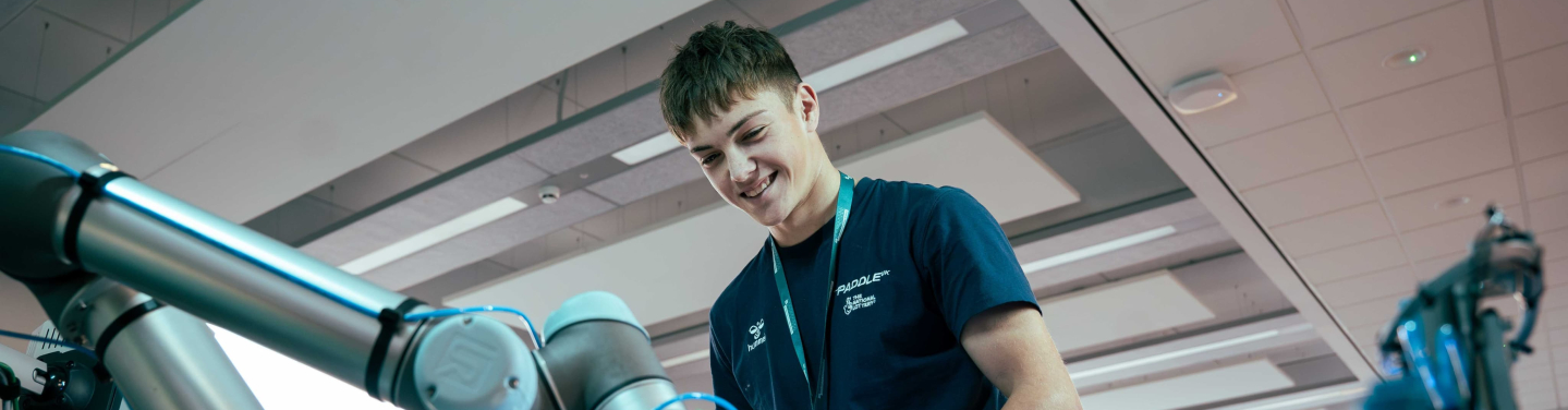 A young man in a blue shirt works with a robotic arm in a modern environment.