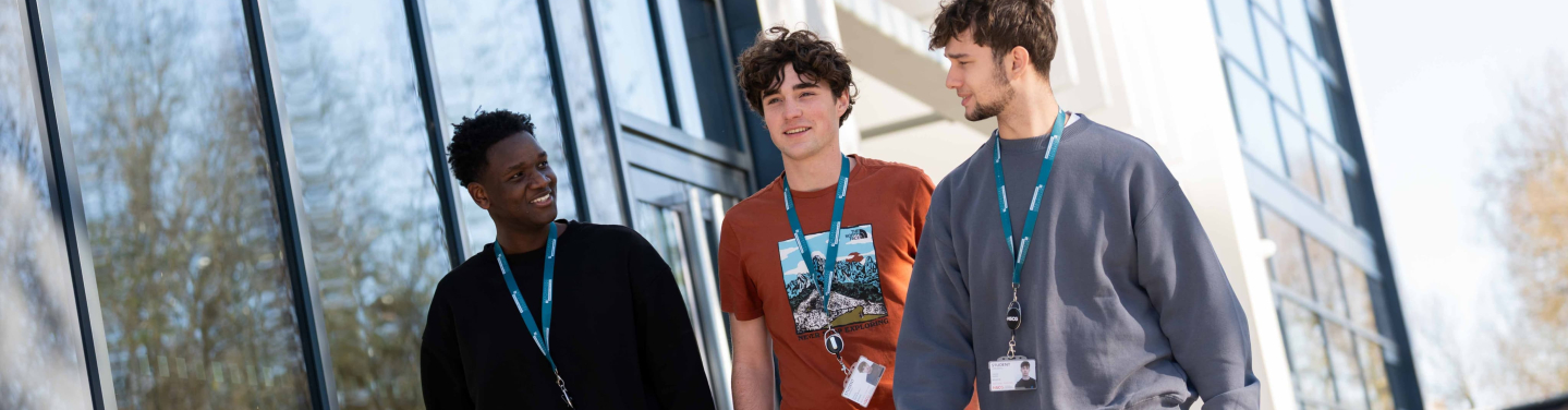 Three students walking together outside a modern building engaged in conversation.