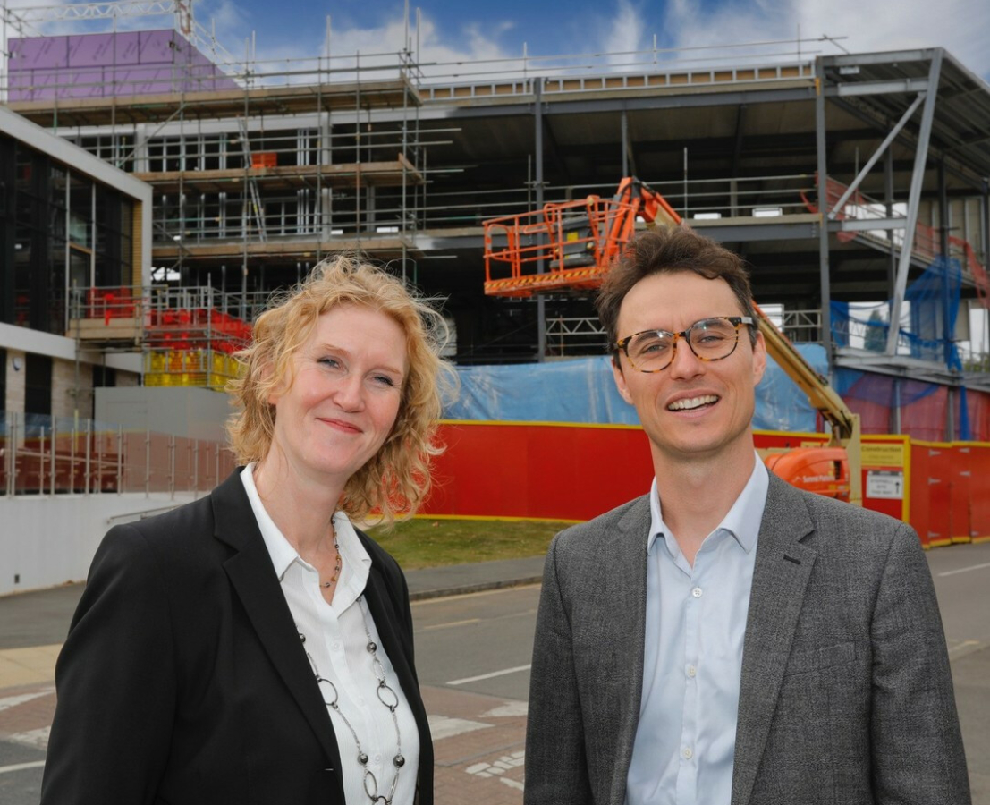 Two individuals stand before a building under construction