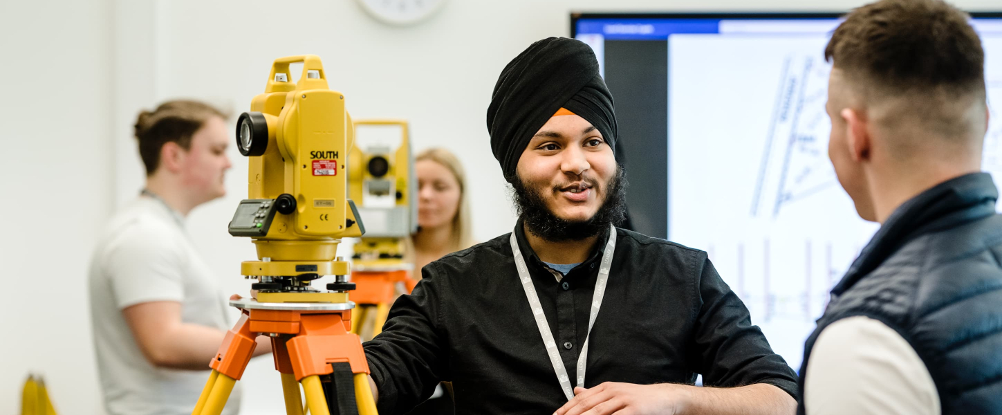 Two people in discussion next to a surveying instrument, with two more people in the background.