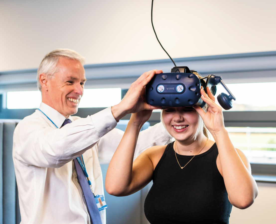 A tutor adjusts a virtual reality headset on a student.